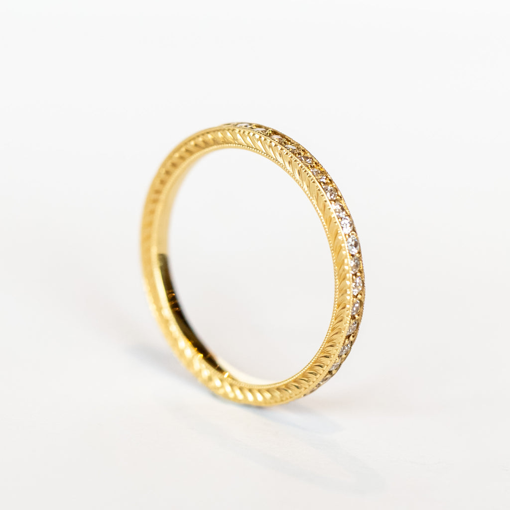 A yellow gold diamond eternity band with a tiny row of diamonds all the way around and engraved sides.
