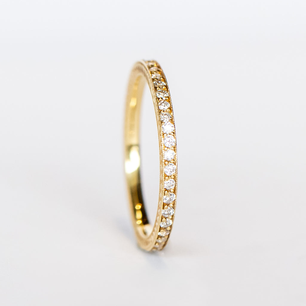 A yellow gold diamond eternity band with a tiny row of diamonds all the way around and engraved sides.