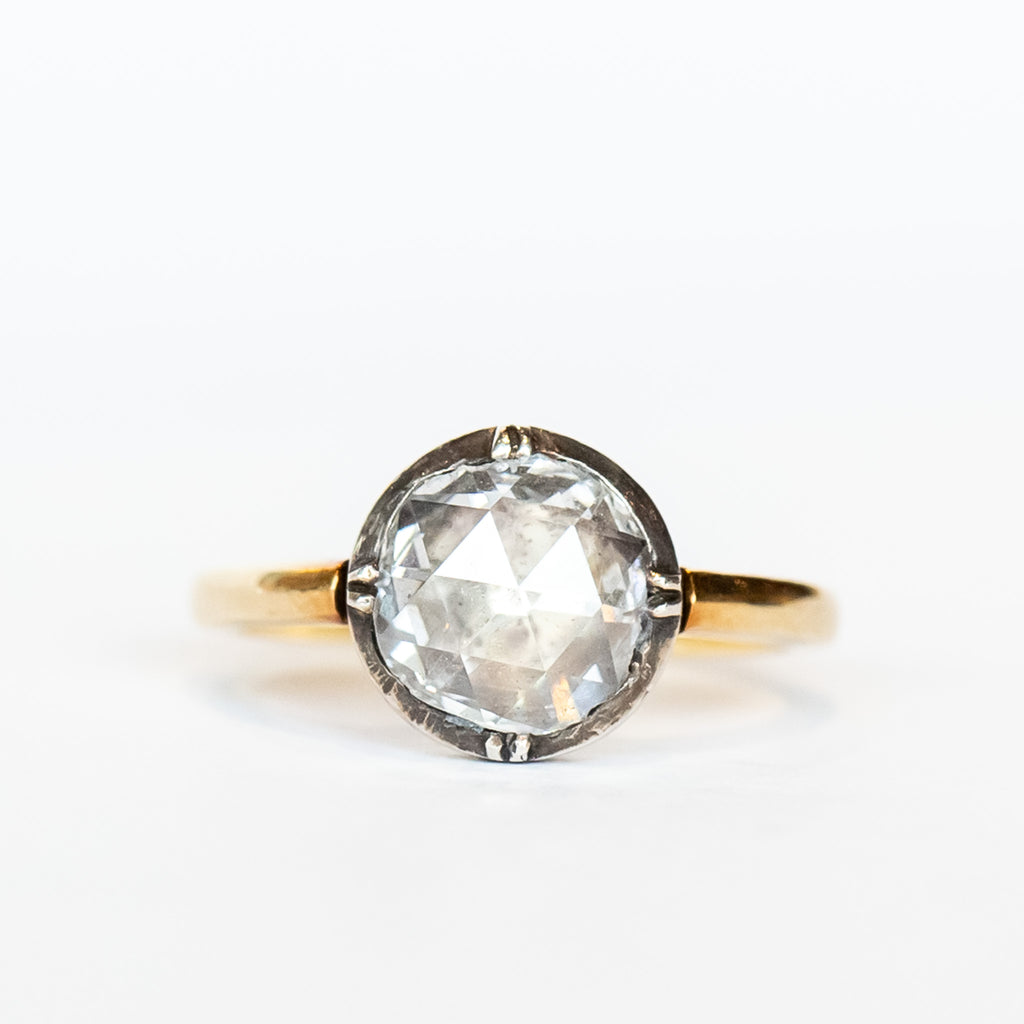 A round rose cut diamond in a sterling silver solitaire prong setting with a yellow gold band.