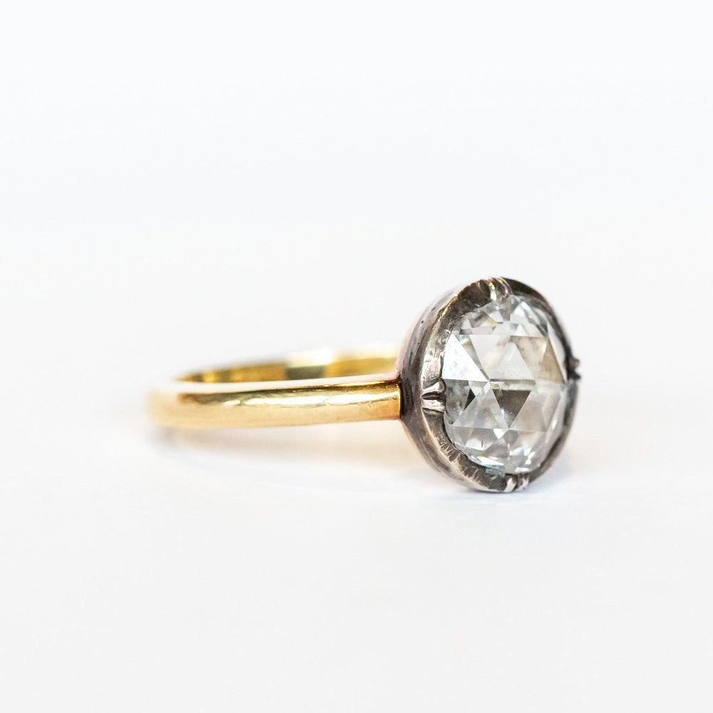 A round rose cut diamond in a sterling silver solitaire prong setting with a yellow gold band.