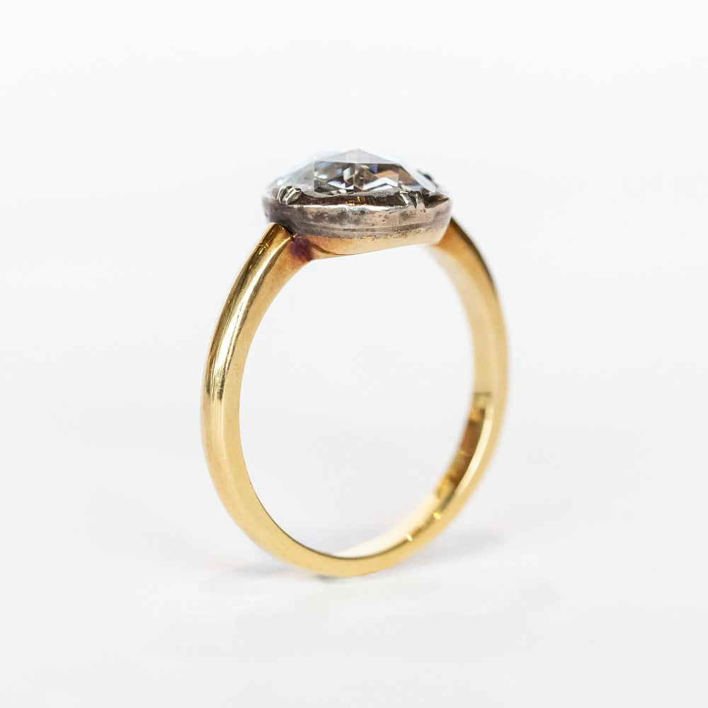 A round rose cut diamond in a sterling silver solitaire prong setting with a yellow gold band.