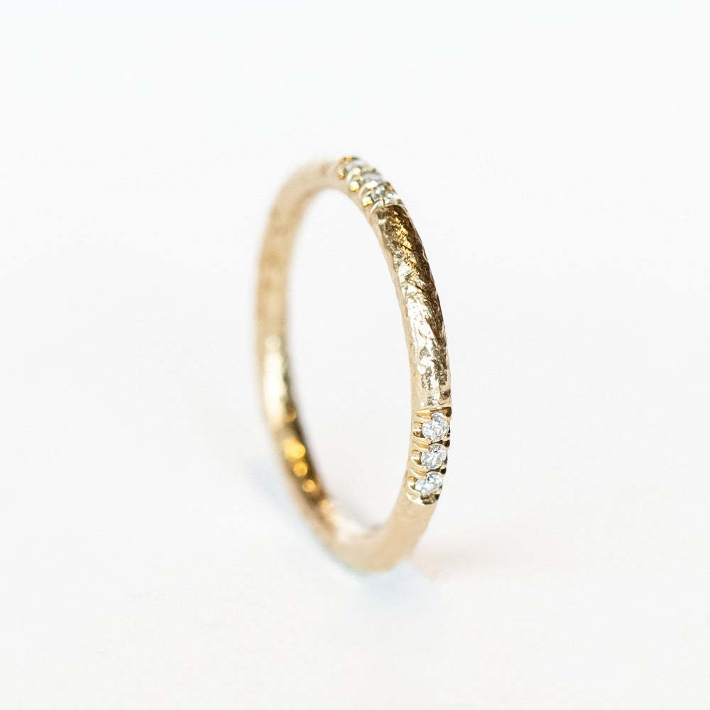 A white gold wedding band with a hammered texture and rows of three-diamonds inlaid in a spaced out design.