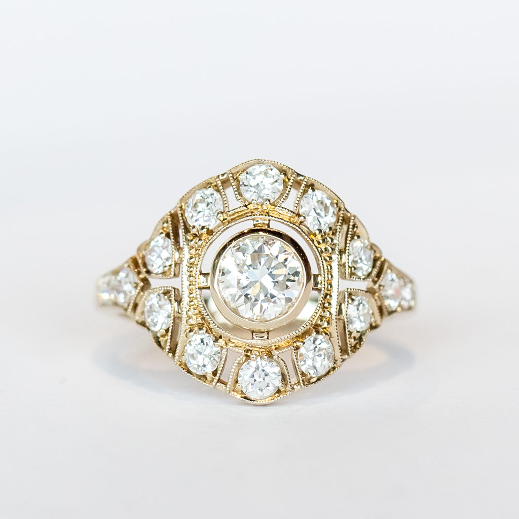 A vintage style diamond engagement ring with a bezel set center stone surrounded by an airy filigree setting and many other diamonds.