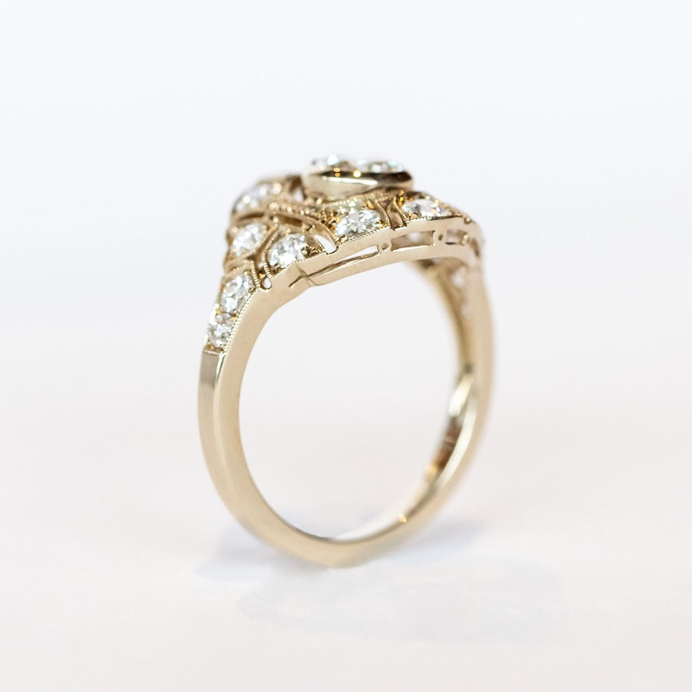 A vintage style diamond engagement ring with a bezel set center stone surrounded by an airy filigree setting and many other diamonds.