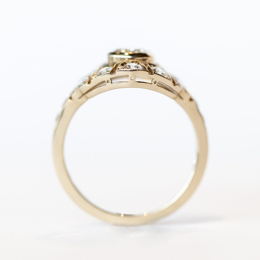 A vintage style diamond engagement ring with a bezel set center stone surrounded by an airy filigree setting and many other diamonds.