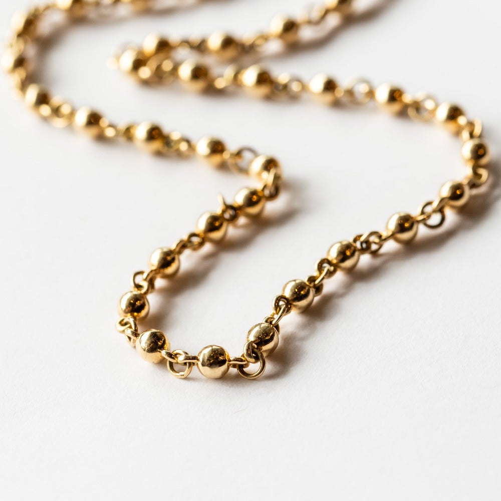 A yellow gold chain necklace made up of spherical links.