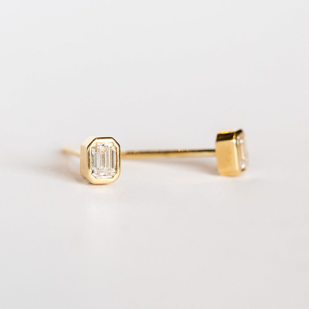 Emerald cut diamond stud earrings set in yellow gold bezels.