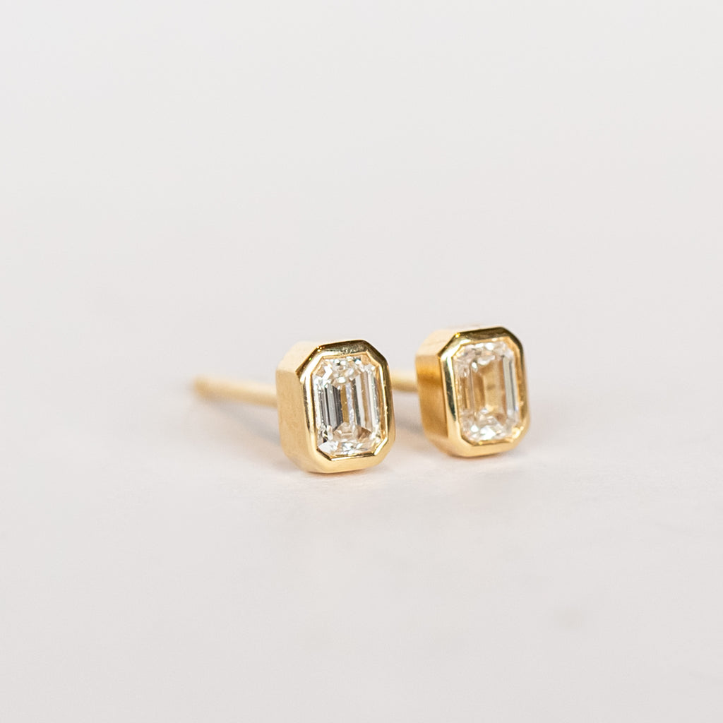 Emerald cut diamond stud earrings set in yellow gold bezels.