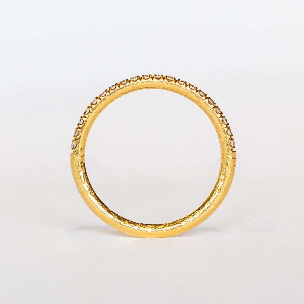 A textured gold wedding band with a row of French pave set diamonds around the top half.
