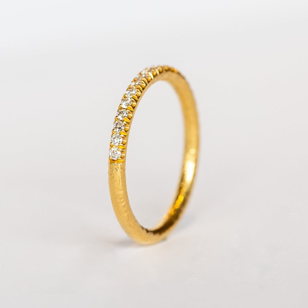 A textured gold wedding band with a row of French pave set diamonds around the top half.