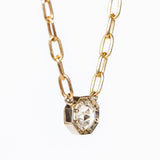 A rose cut diamond set in an octagonal white gold mounting centered on a yellow gold paperclip chain necklace.