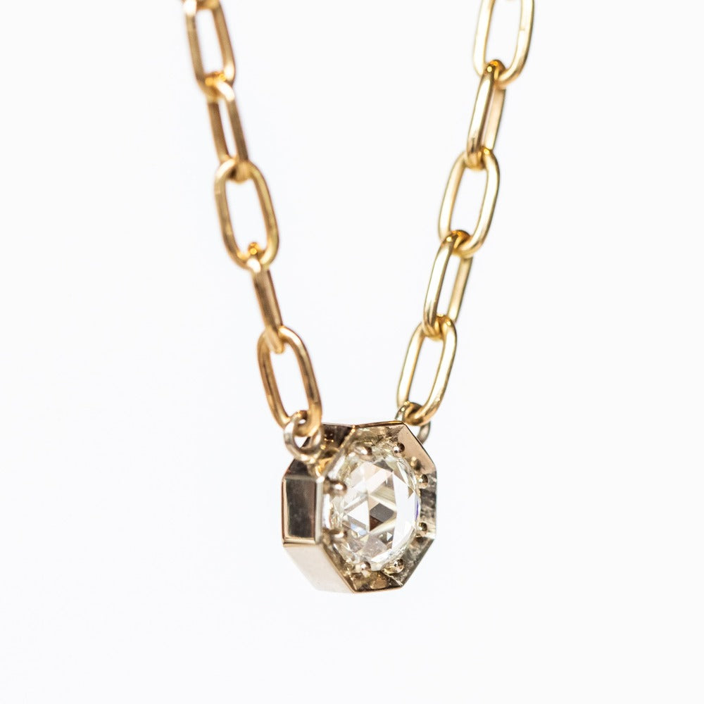 A rose cut diamond set in an octagonal white gold mounting centered on a yellow gold paperclip chain necklace.