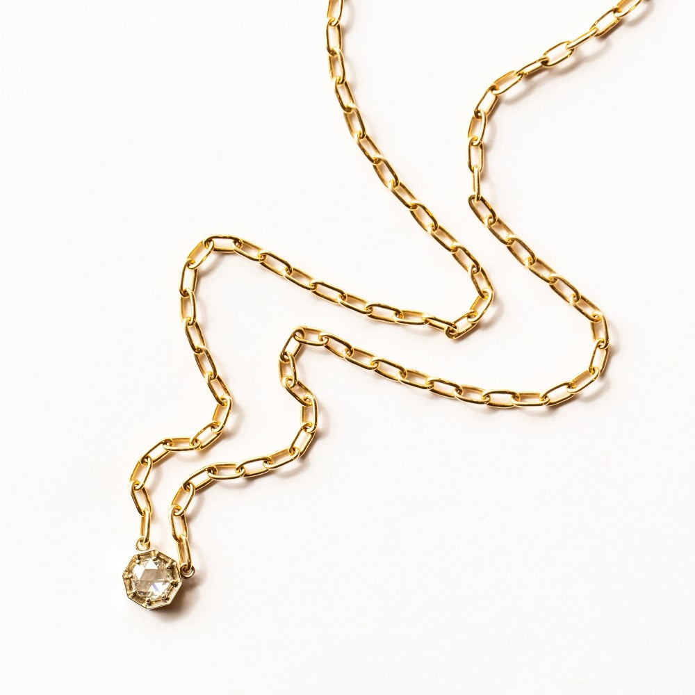 A rose cut diamond set in an octagonal white gold mounting centered on a yellow gold paperclip chain necklace.