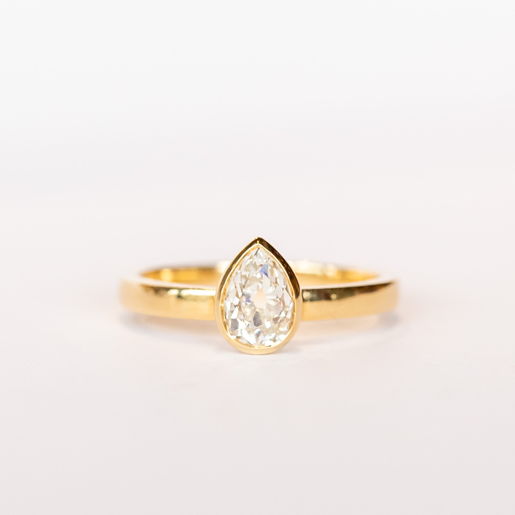 A pear-shaped diamond is bezel set in yellow gold on a solitaire engagement ring.