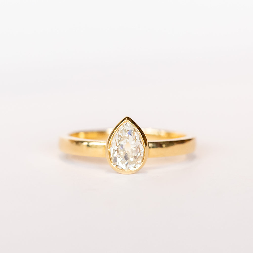A pear-shaped diamond is bezel set in yellow gold on a solitaire engagement ring.