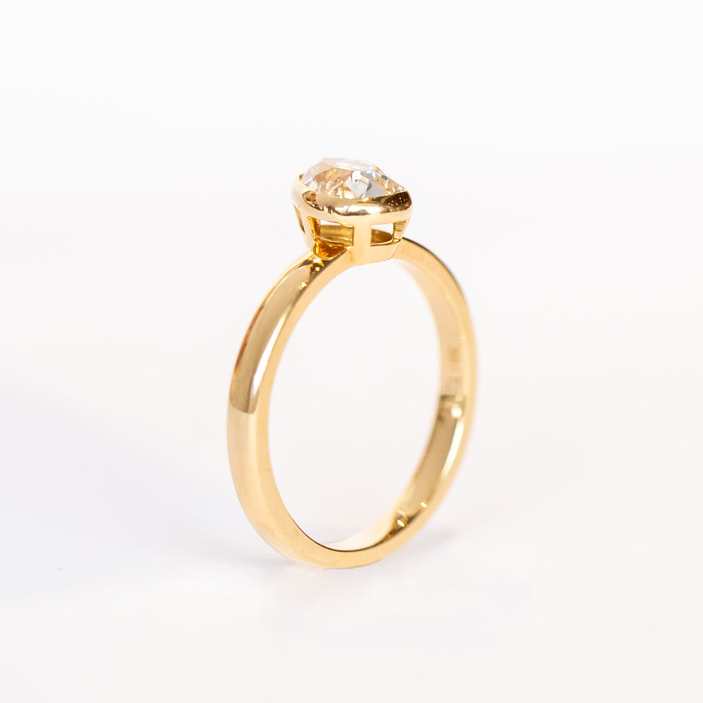 A pear-shaped diamond is bezel set in yellow gold on a solitaire engagement ring.