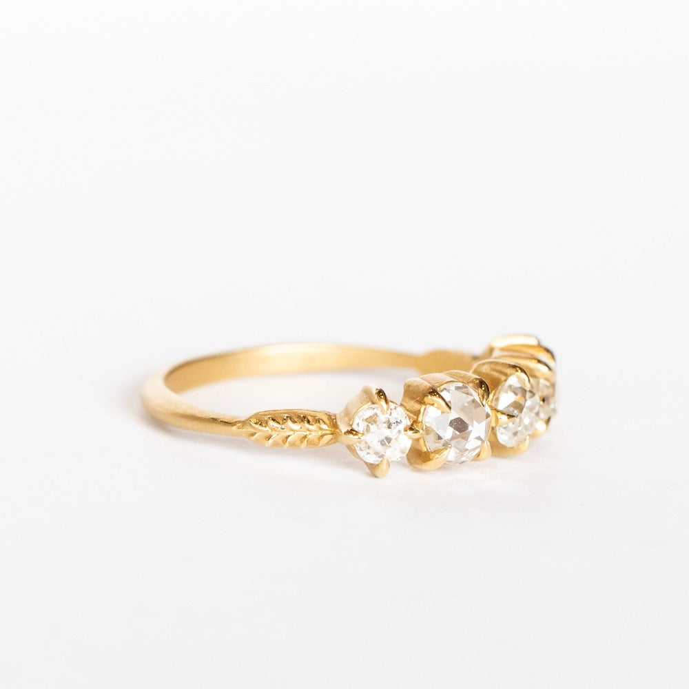 A yellow gold wedding band featuring five mixed-cut diamonds prong set with leaf-like accents on each side.