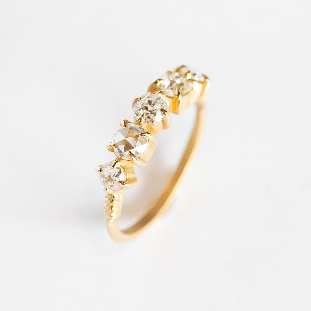 A yellow gold wedding band featuring five mixed-cut diamonds prong set with leaf-like accents on each side.