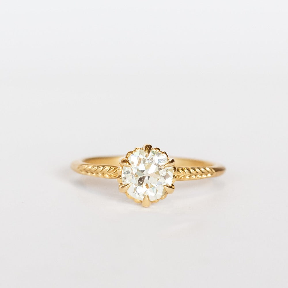 A yellow gold solitaire diamond engagement ring featuring a prong set old european cut diamond and a slender matte finish, leaf accented band.