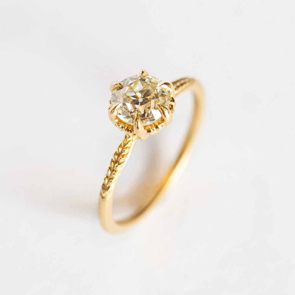 A yellow gold solitaire diamond engagement ring featuring a prong set old european cut diamond and a slender matte finish, leaf accented band.