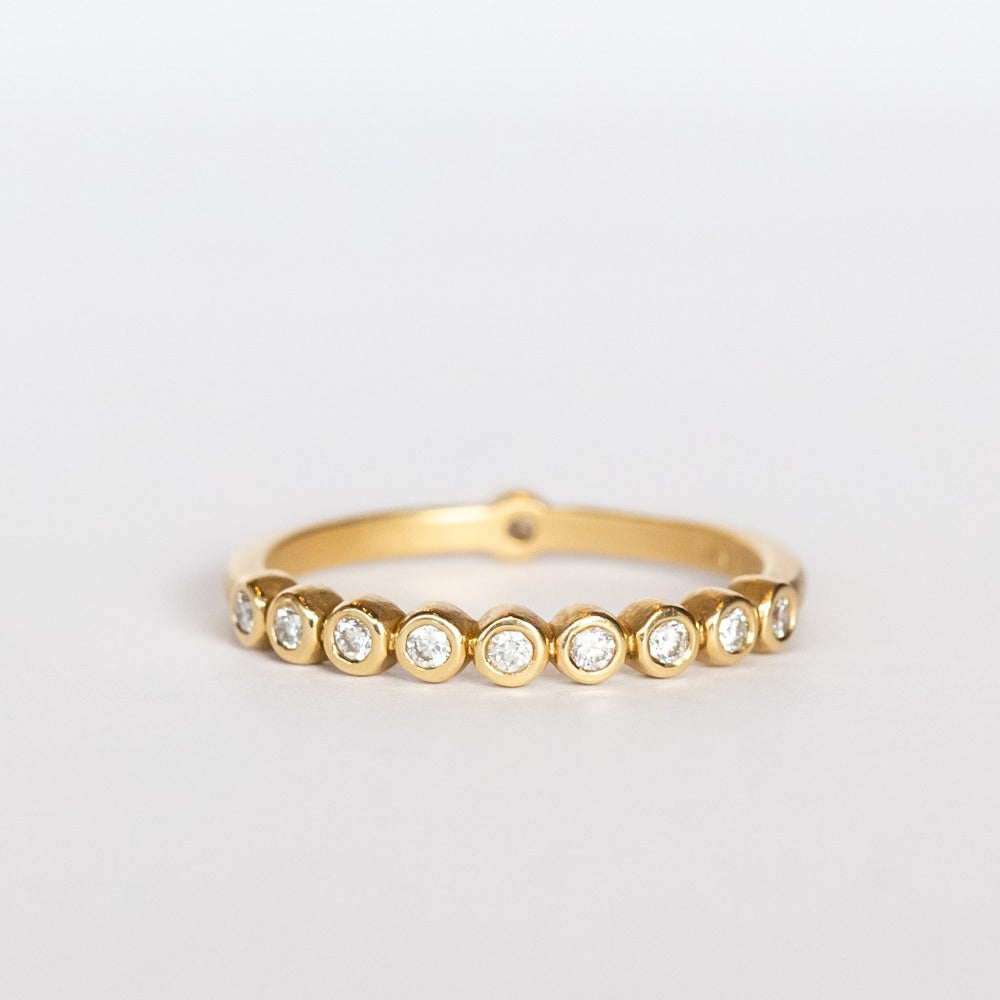 A yellow gold wedding band featuring a row of small bezel set diamonds across the top with one at the very center base of the band.