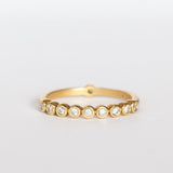 A yellow gold wedding band featuring a row of small bezel set diamonds across the top with one at the very center base of the band.
