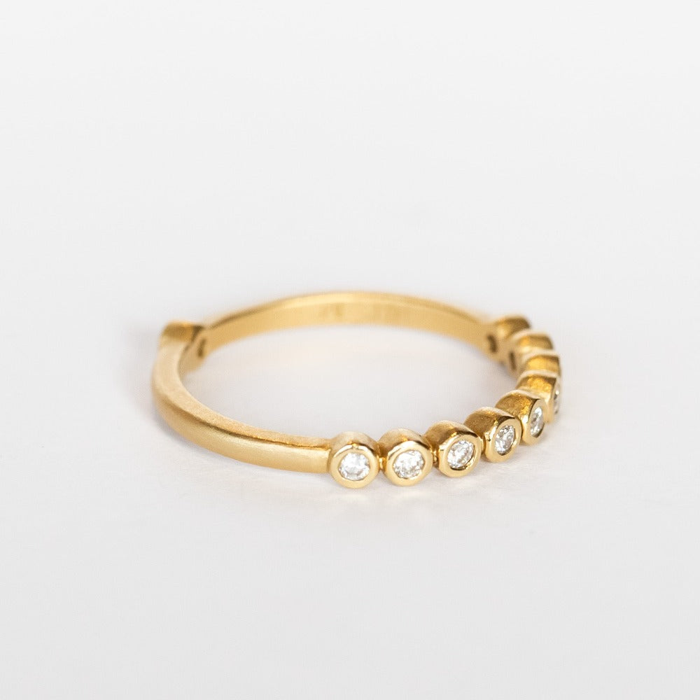 A yellow gold wedding band featuring a row of small bezel set diamonds across the top with one at the very center base of the band.