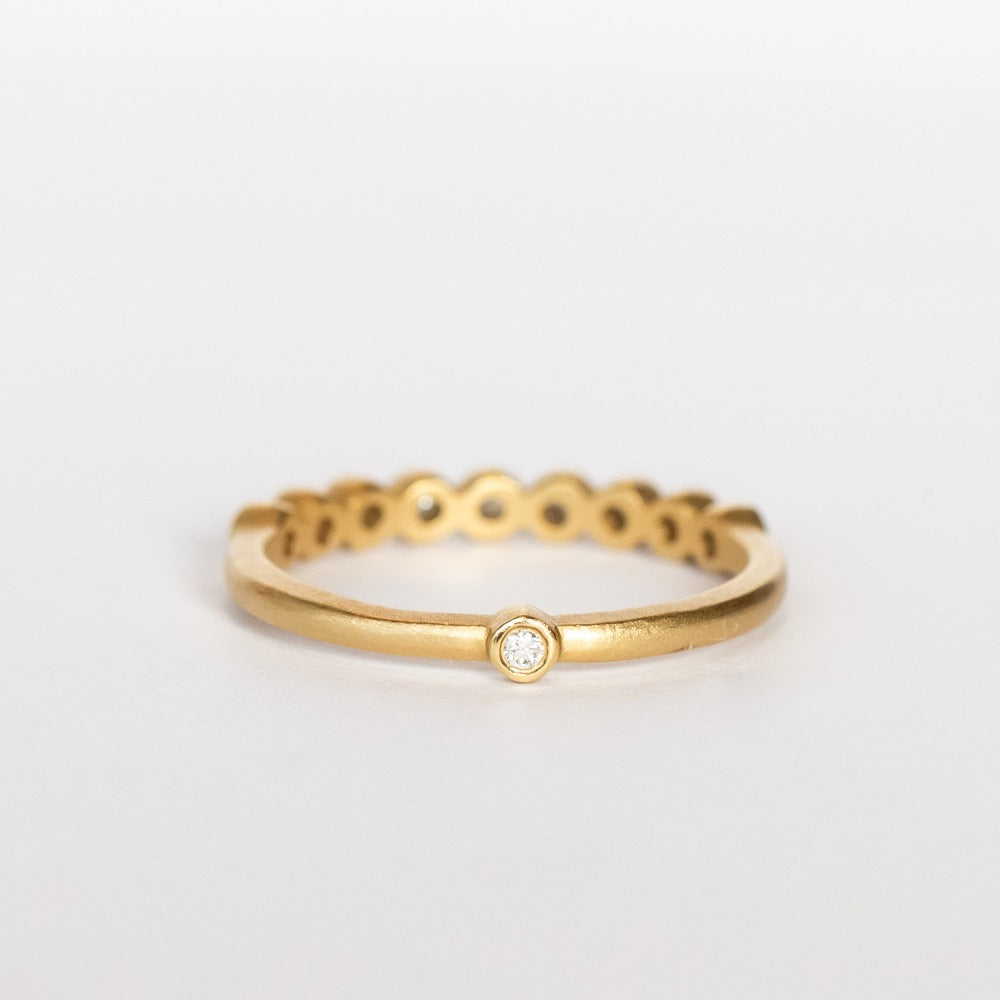 A yellow gold wedding band featuring a row of small bezel set diamonds across the top with one at the very center base of the band.