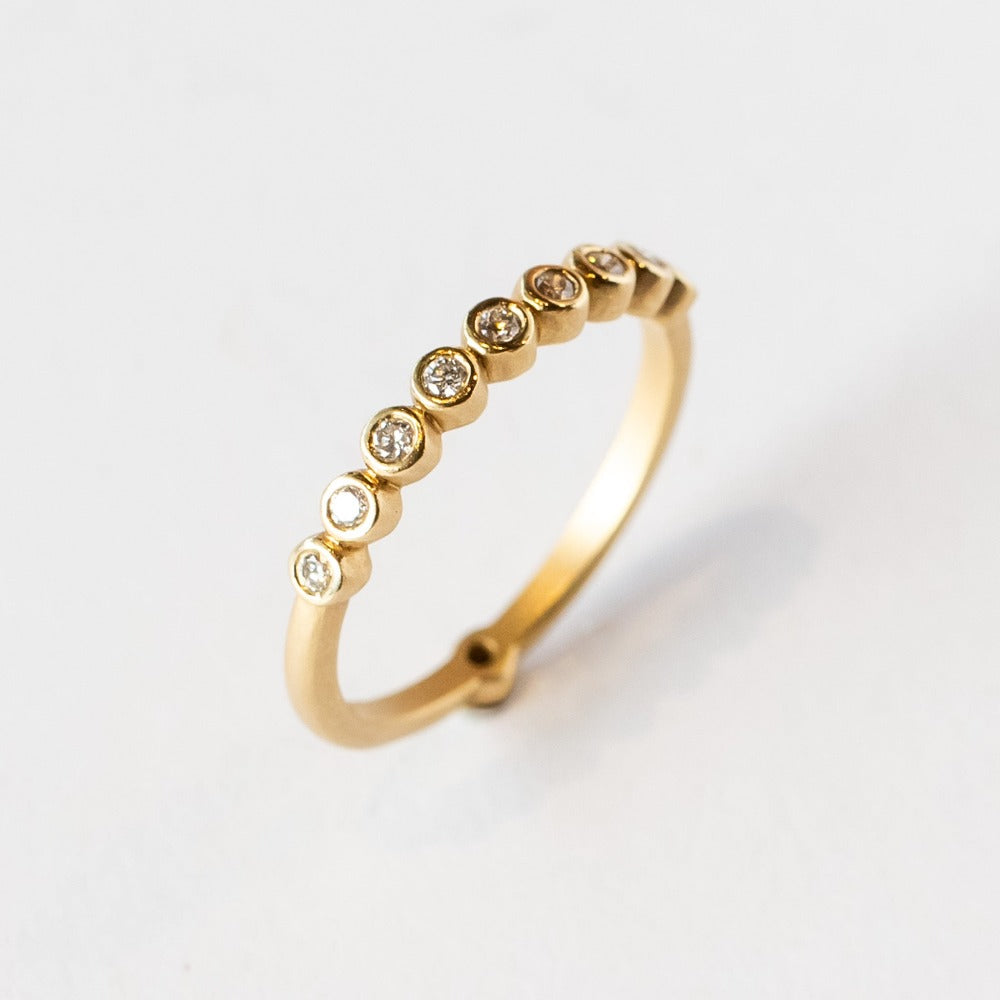 A yellow gold wedding band featuring a row of small bezel set diamonds across the top with one at the very center base of the band.
