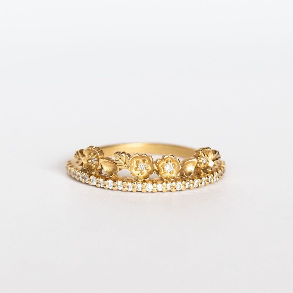 A yellow gold band with a slender row of diamonds topped with a floral tiara on one side. The small flowers and leaves are dotted with additional diamonds.
