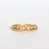 A yellow gold band with a slender row of diamonds topped with a floral tiara on one side. The small flowers and leaves are dotted with additional diamonds.