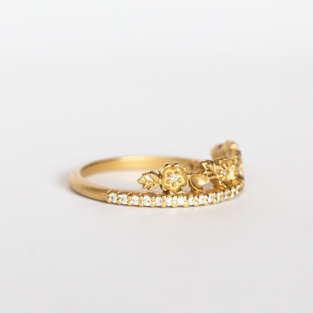 A yellow gold band with a slender row of diamonds topped with a floral tiara on one side. The small flowers and leaves are dotted with additional diamonds.