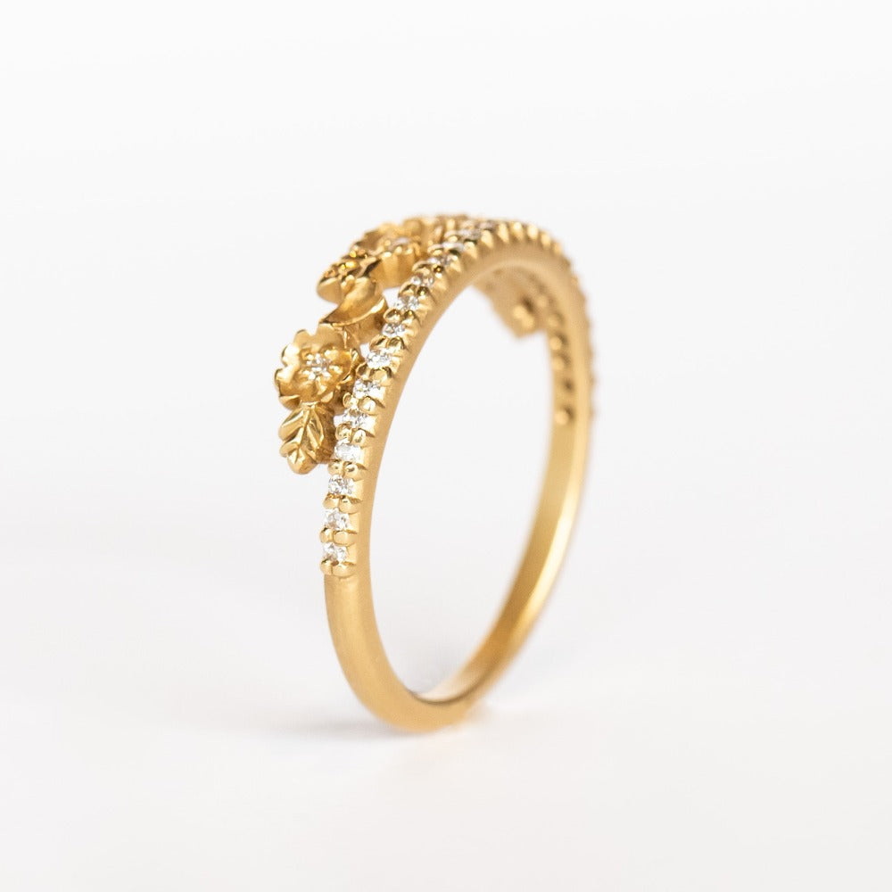 A yellow gold band with a slender row of diamonds topped with a floral tiara on one side. The small flowers and leaves are dotted with additional diamonds.
