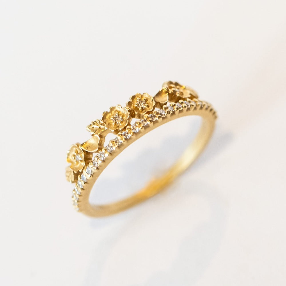 A yellow gold band with a slender row of diamonds topped with a floral tiara on one side. The small flowers and leaves are dotted with additional diamonds.