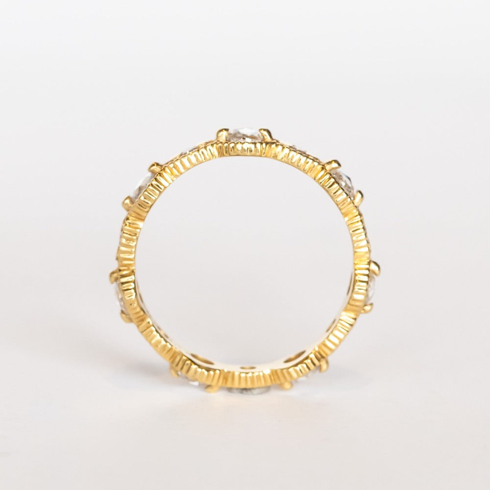 A yellow gold eternity band featuring round rose cut diamonds alternating with tiny brilliant round white diamonds. The alternating round and oval settings are accented with milgrain bed details.