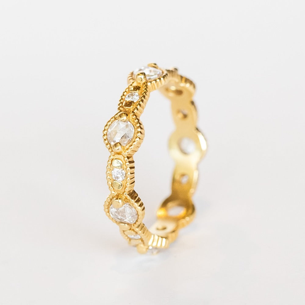 A yellow gold eternity band featuring round rose cut diamonds alternating with tiny brilliant round white diamonds. The alternating round and oval settings are accented with milgrain bed details.