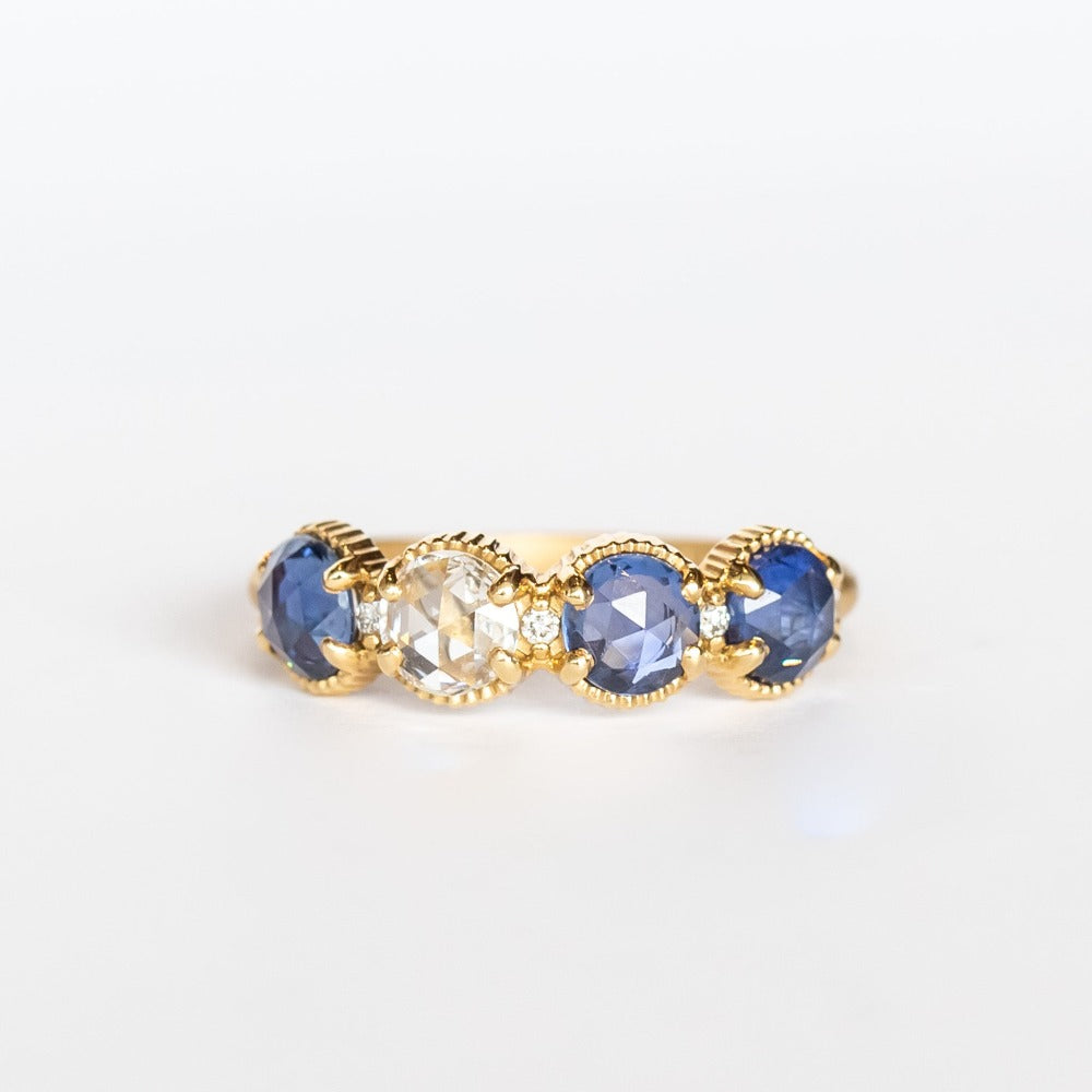 A yellow gold band set with three rose cut blue sapphires and one rose cut diamond. There are tiny white diamonds in between each stone and the settings are edged with bead details.