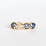 A yellow gold band set with three rose cut blue sapphires and one rose cut diamond. There are tiny white diamonds in between each stone and the settings are edged with bead details.