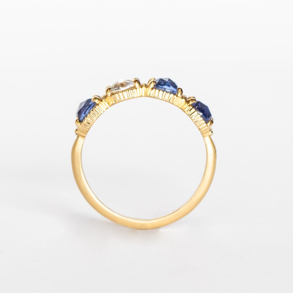 A yellow gold band set with three rose cut blue sapphires and one rose cut diamond. There are tiny white diamonds in between each stone and the settings are edged with bead details.