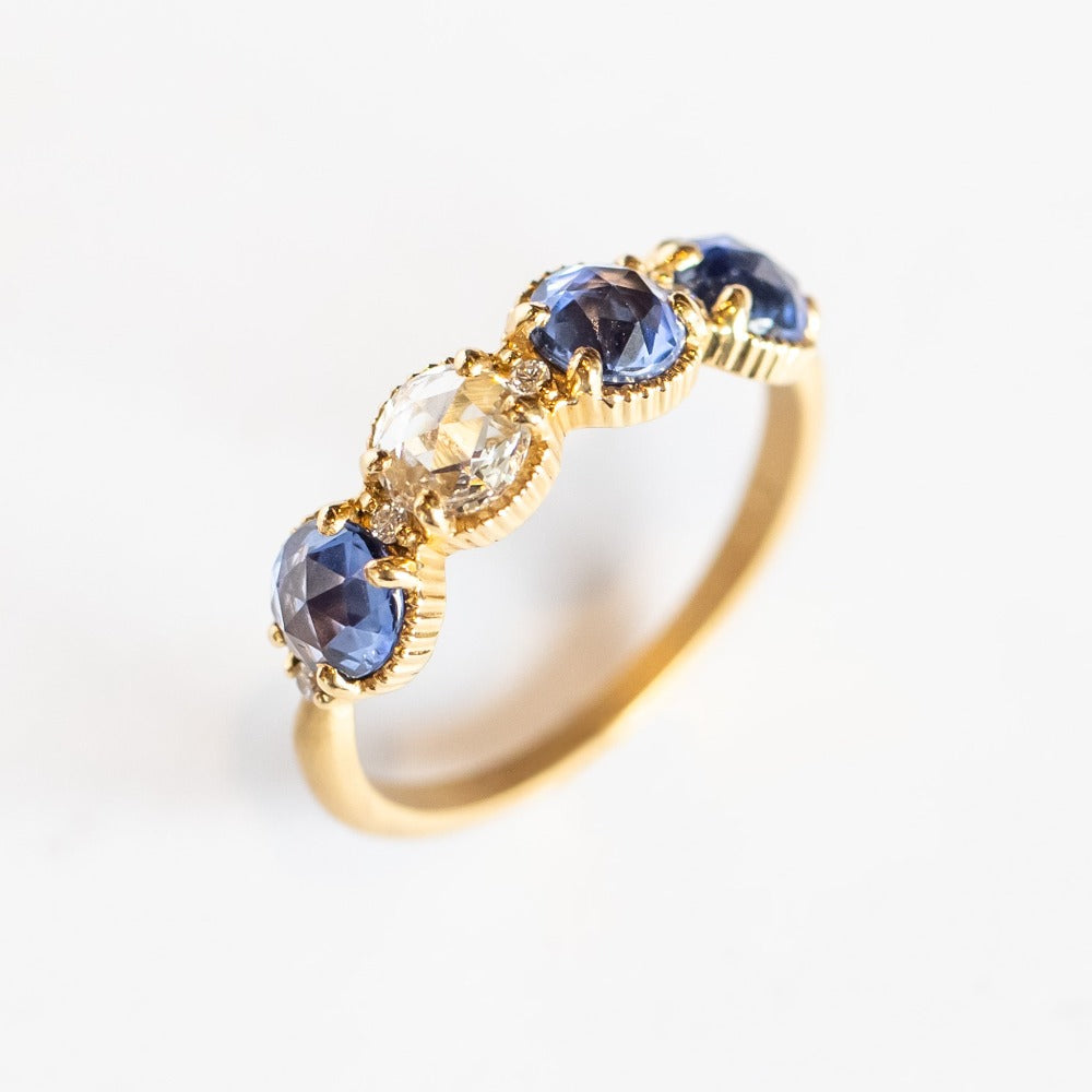 A yellow gold band set with three rose cut blue sapphires and one rose cut diamond. There are tiny white diamonds in between each stone and the settings are edged with bead details.