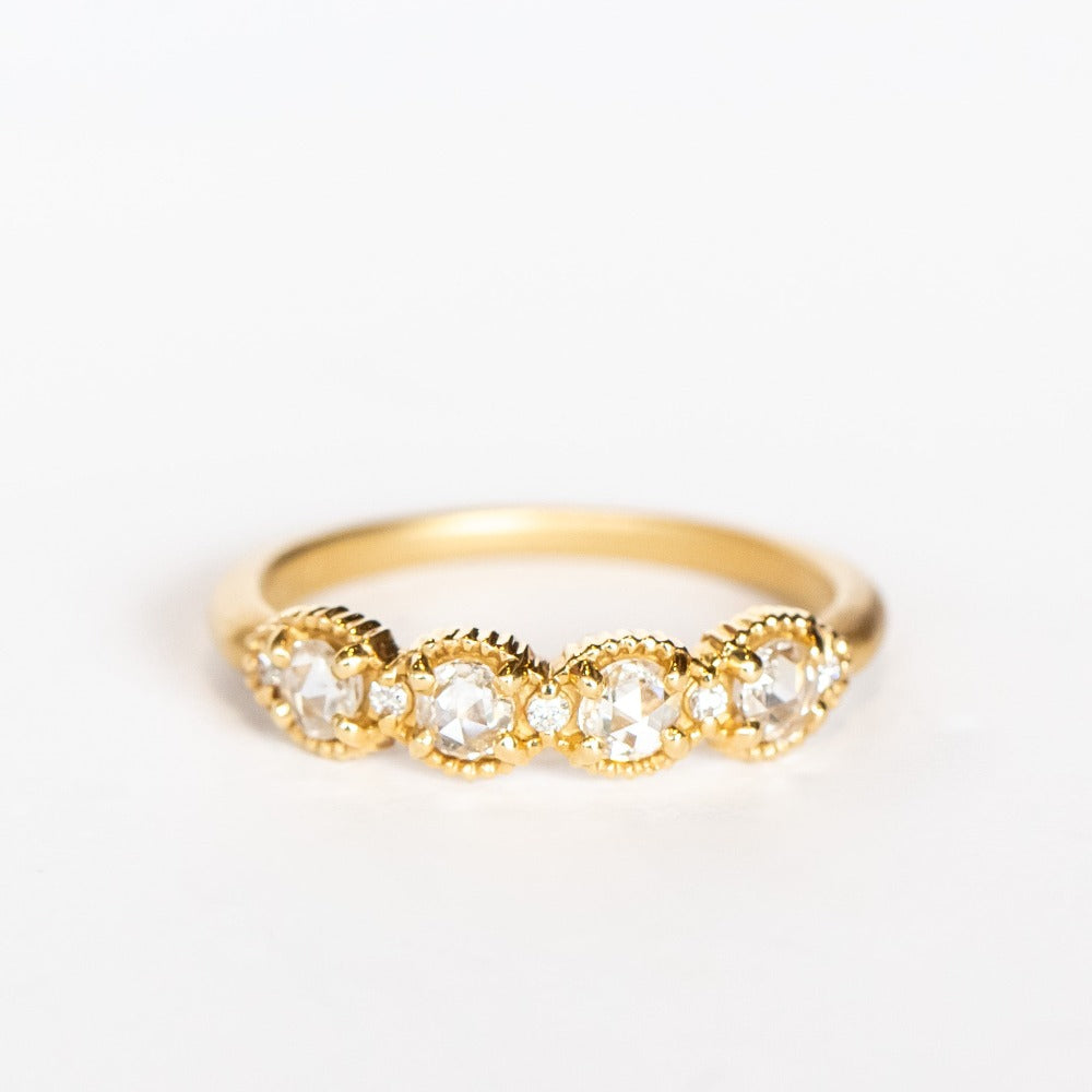 A yellow gold band set with four round rose cut white diamonds alternating with tiny brilliant white diamonds. The edges of the setting have bead details.