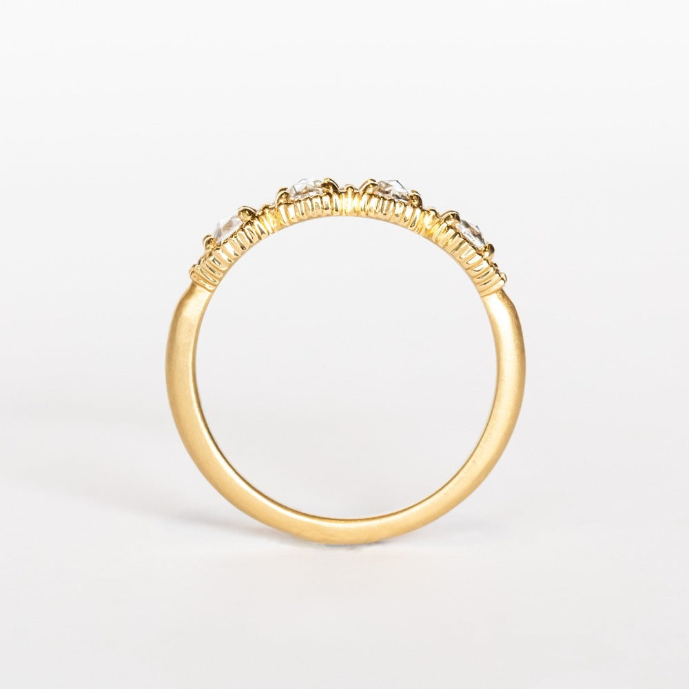 A yellow gold band set with four round rose cut white diamonds alternating with tiny brilliant white diamonds. The edges of the setting have bead details.