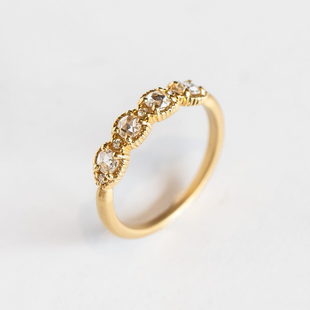 A yellow gold band set with four round rose cut white diamonds alternating with tiny brilliant white diamonds. The edges of the setting have bead details.
