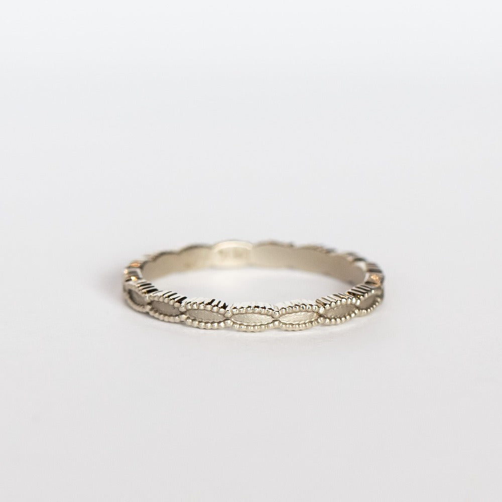 A white gold wedding band with a seed-shaped pattern all the way around. The edges have milgrain beading.
