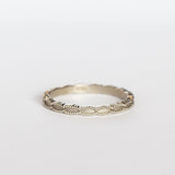 A white gold wedding band with a seed-shaped pattern all the way around. The edges have milgrain beading.
