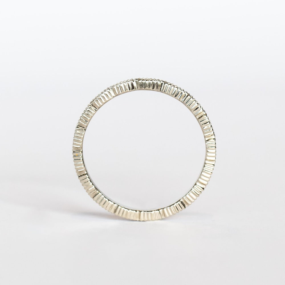 A white gold wedding band with a seed-shaped pattern all the way around. The edges have milgrain beading.