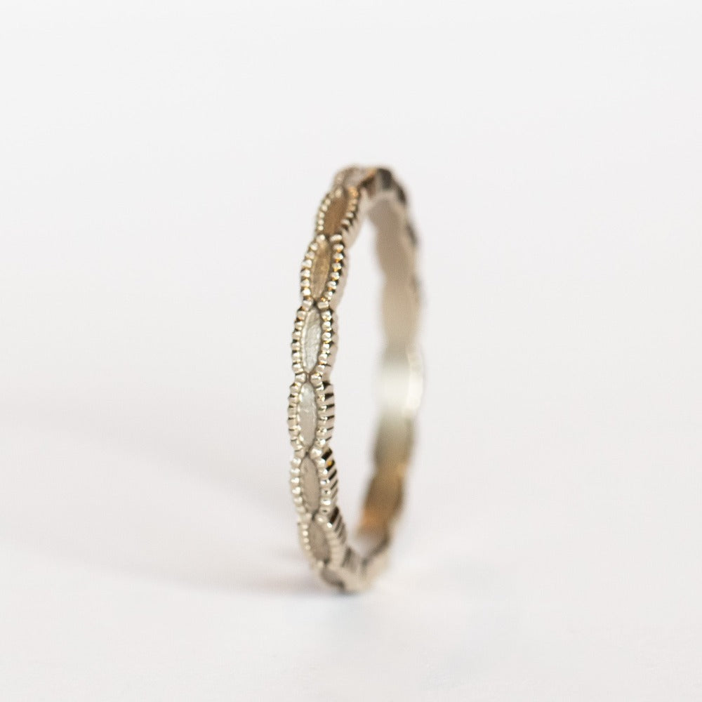 A white gold wedding band with a seed-shaped pattern all the way around. The edges have milgrain beading.