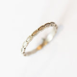 A white gold wedding band with a seed-shaped pattern all the way around. The edges have milgrain beading.