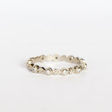 A white gold eternity wedding band featuring leaf patterns alternating with tiny bezel set diamonds surrounded with milgrain dot accents.
