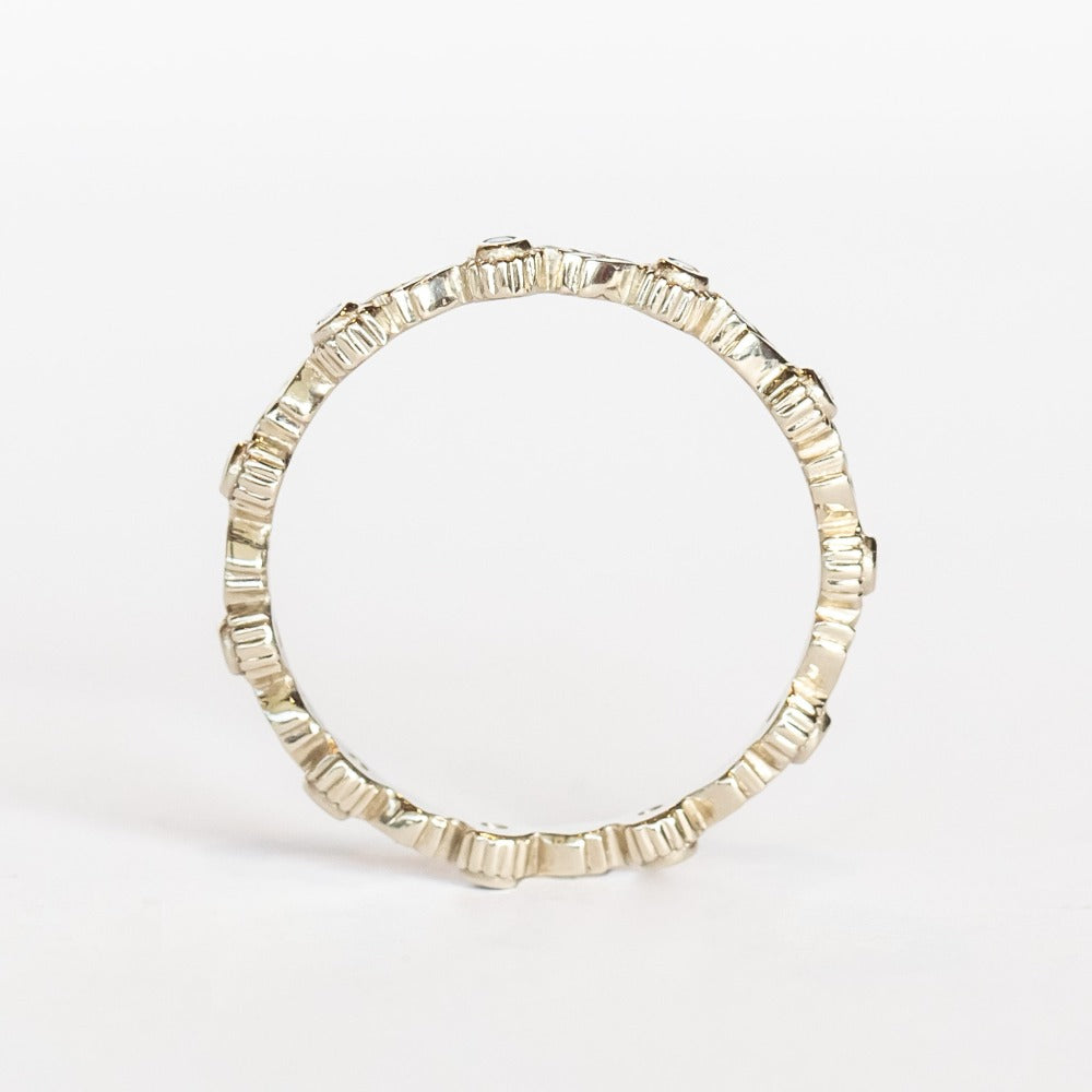 A white gold eternity wedding band featuring leaf patterns alternating with tiny bezel set diamonds surrounded with milgrain dot accents.